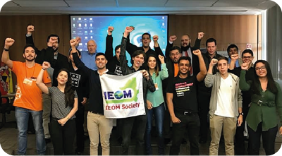 2º South American ieom Brazil conference – prêmio destaque de liderança. Um grupo de jovens posa para foto com o punho fechado erguido. Na frente, seguram um banner do evento.