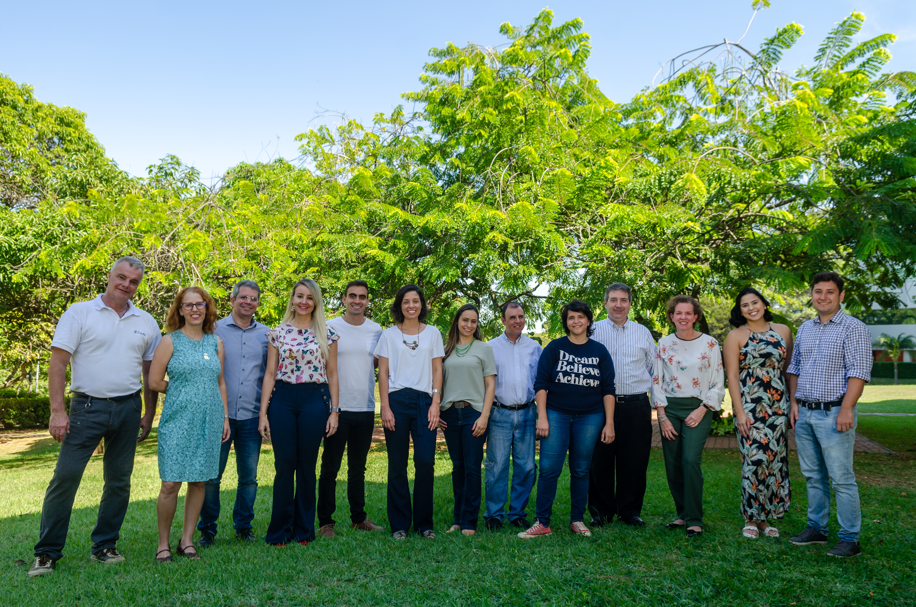 Foto em dia de sol o comitê de sustentabilidade posa em pé lado a lado no gramado bem arborizado da Facens.