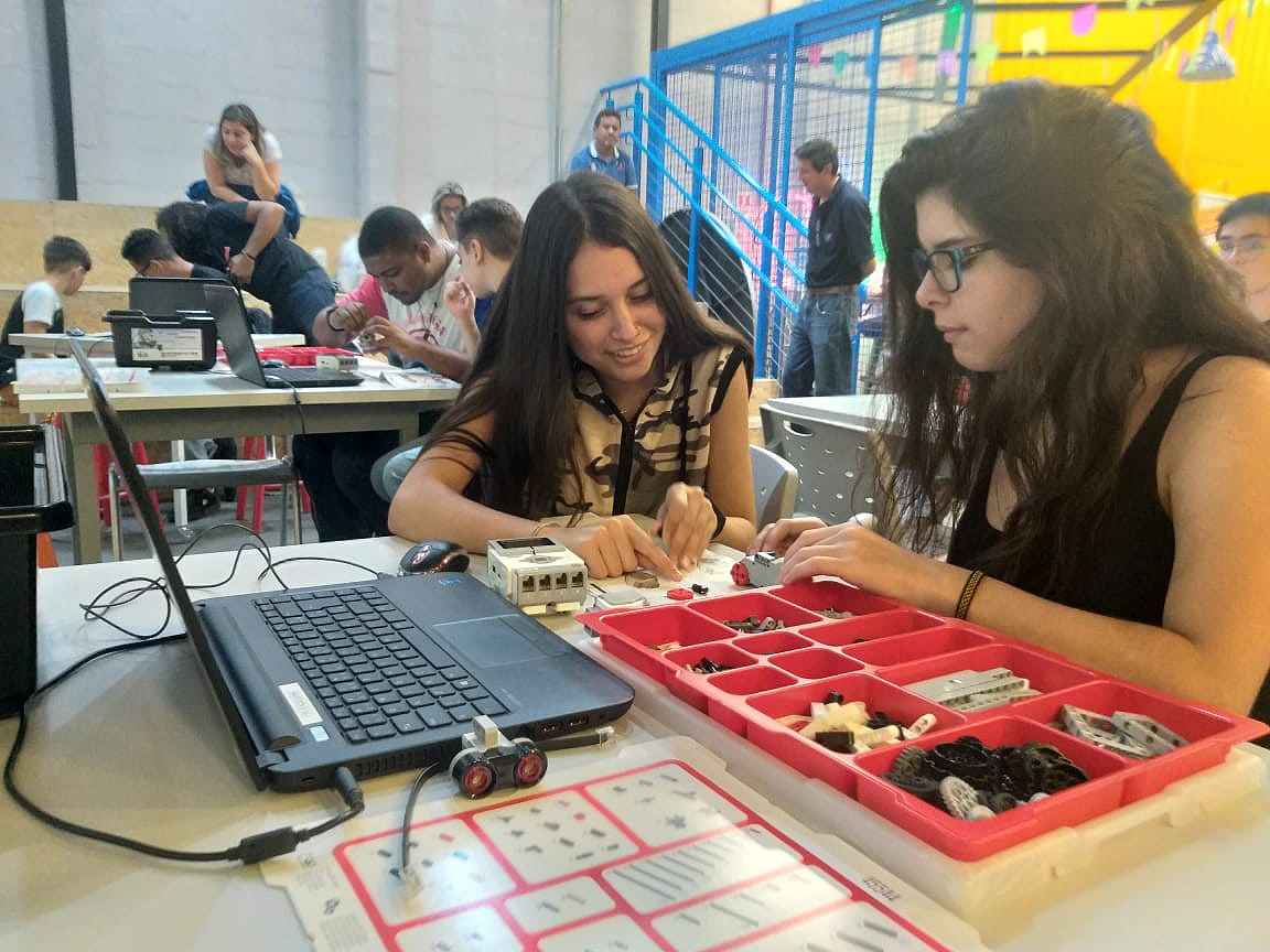 Foto dos alunos em mesas junto ao notes e caixas plásticas com divisórias organizadoras com material.