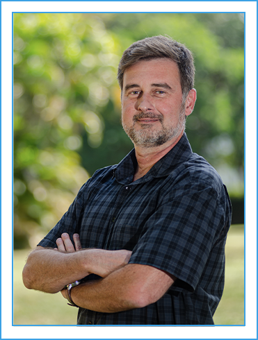 Foto de Lester Faria, diretor de pesquisa. Pessoa de meia idade de pele branca, cabelos, bigode e barba grisalhos, usa camisa de manga curta xadrez, posa com os braços cruzados.