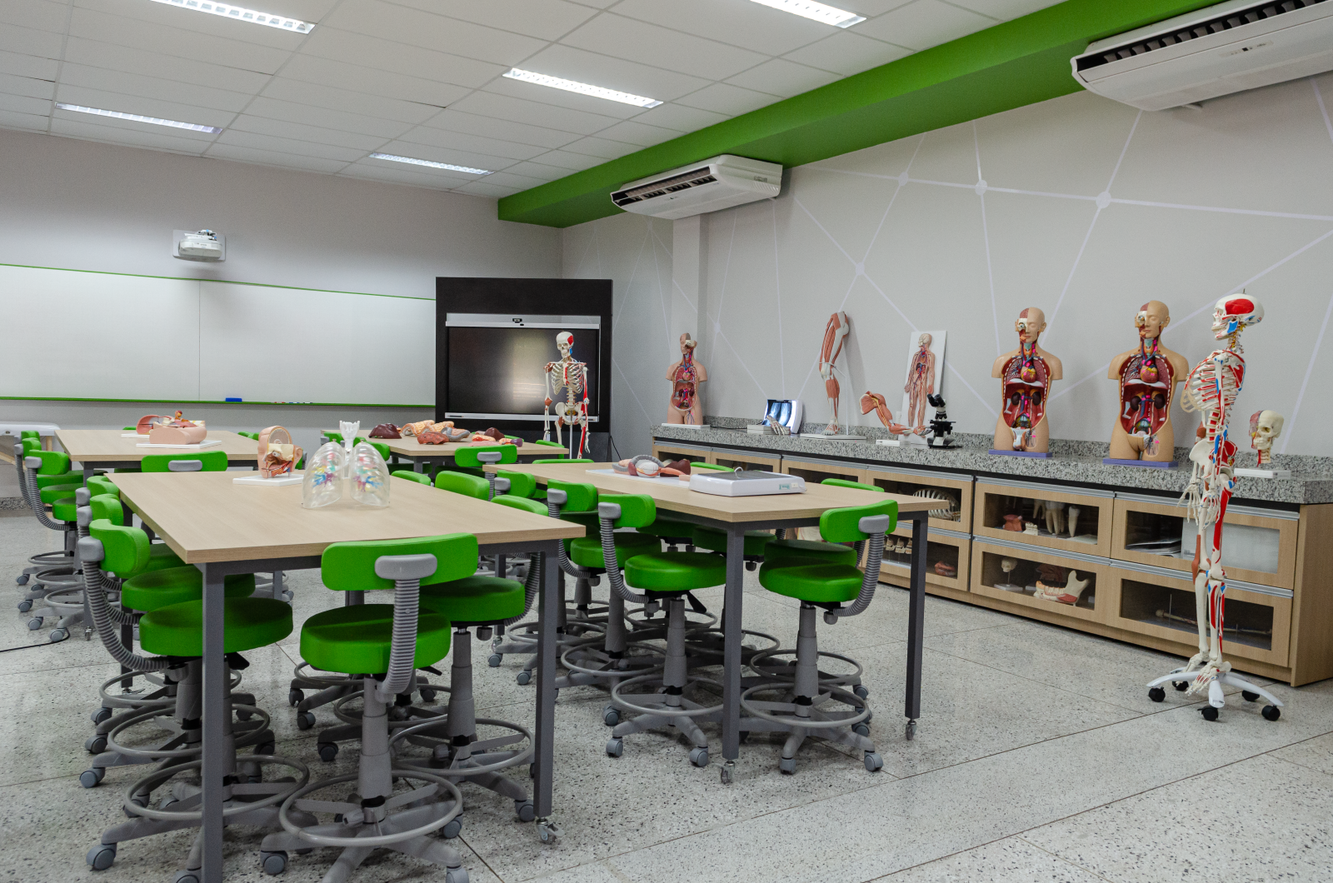 laboratório de saúde com mesas claras e cadeiras giratórias estilo banqueta com encosto em verde cítrico. Sobre a bancada modelos de anatomia.