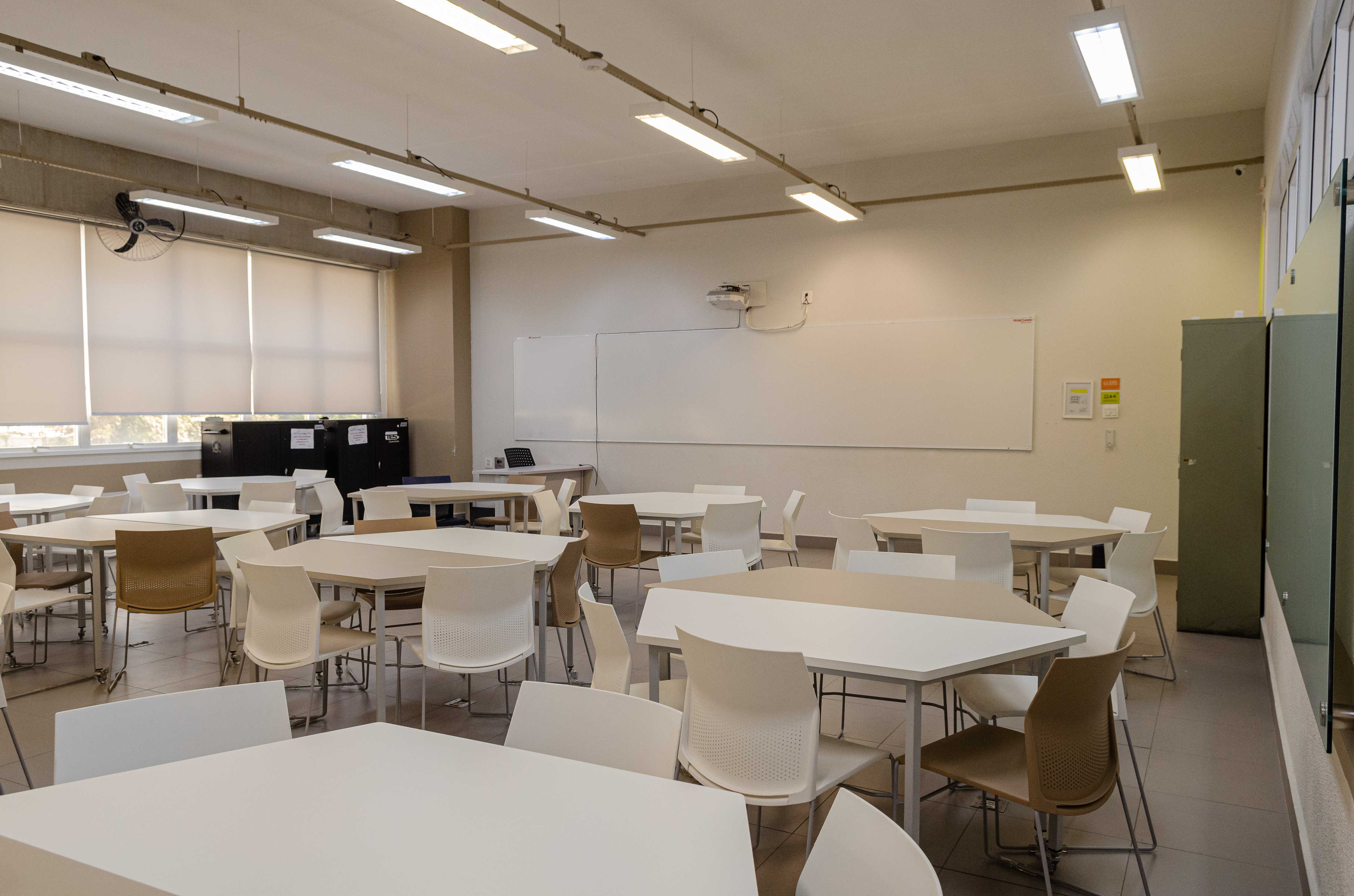 Sala de aulas invertida em tons claros com mesas retangulares e cadeiras ergonômicas ao redor.