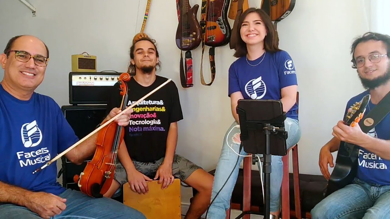 Foto na sala de criação. 4 pessoas, entre alunos e professores junto aos instrumentos, 3 usam a camiseta azul do Facens Musical.