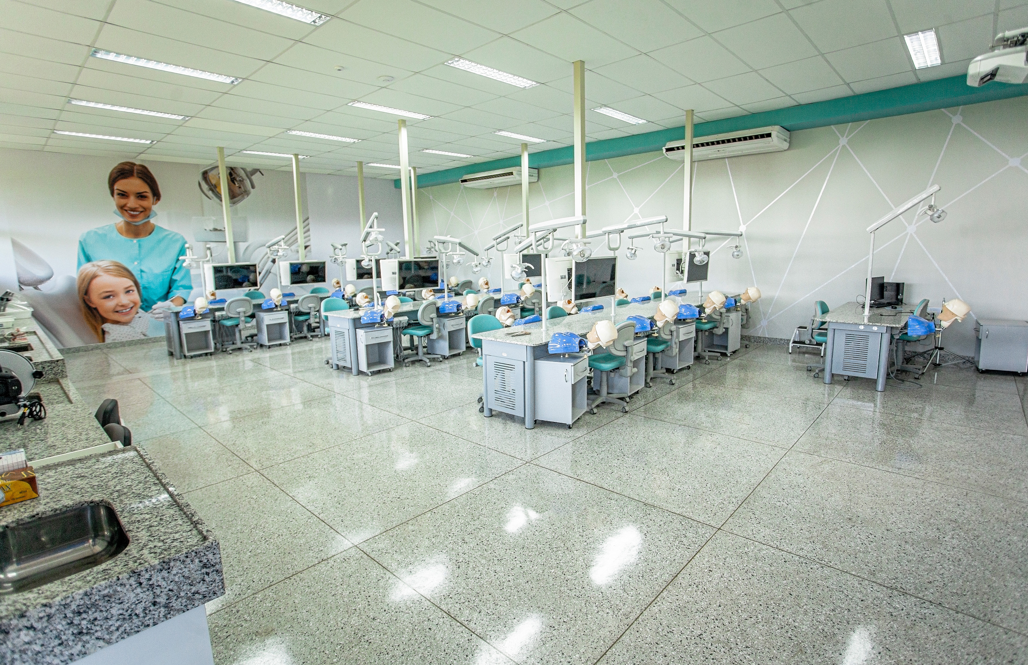 laboratório de odontologia. Equipado em cores claras, em tons de verde e azul. No painel foto de uma criança sorridente na cadeira odontológica sendo atendida por profissional.