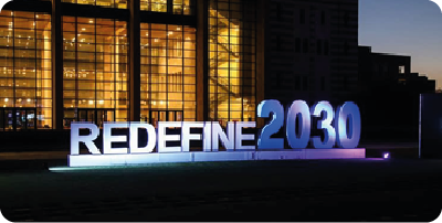 2021 Real Life Challenge 2021. Foto noturna da fachada de um prédio com acabamento espelhado em dourado, na frente da fachada, lê-se: redefine 2030.